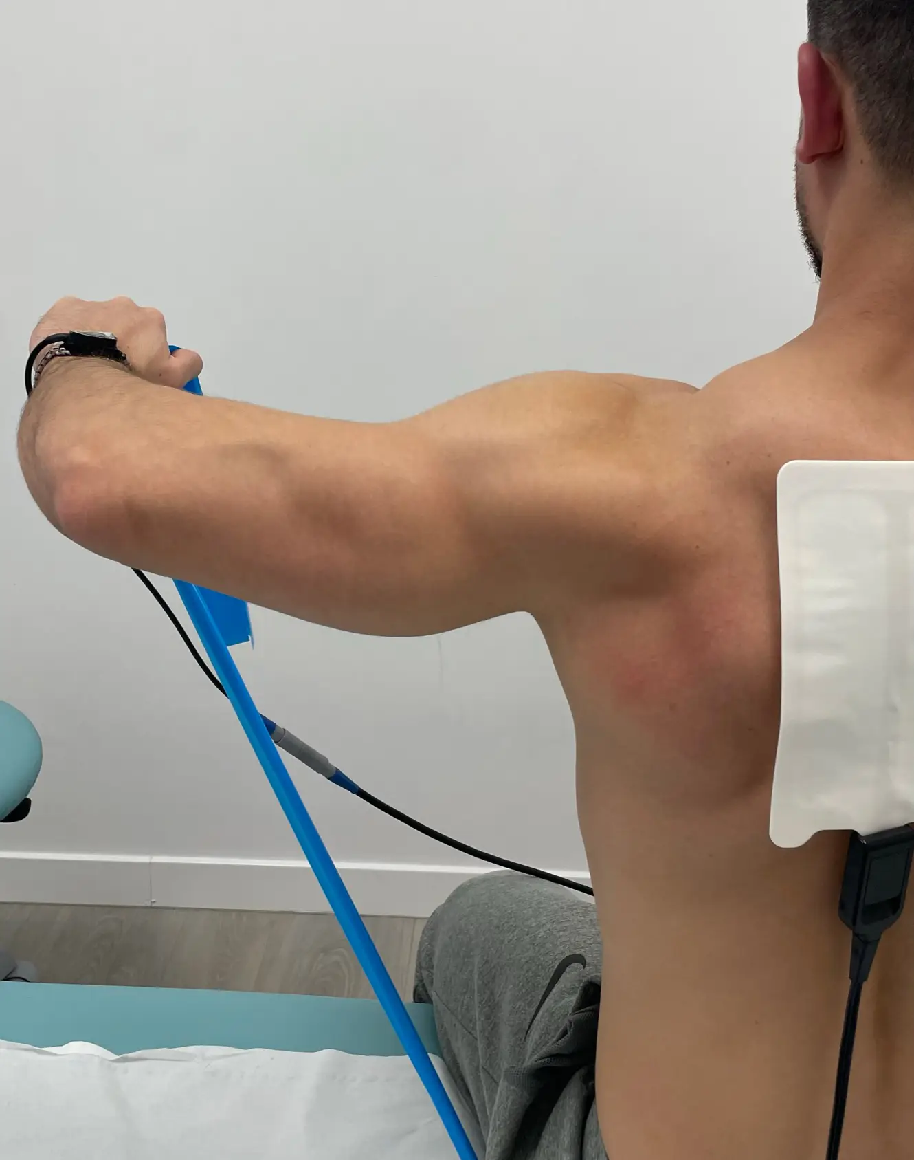 Paciente realizando ejercicio de rehabilitación de hombro con banda elástica y electroestimulación en nuestra clínica de Rivas